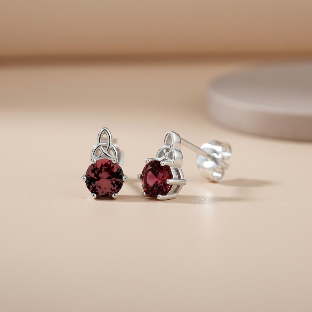Sterling silver Celtic stud earrings with simulated rubies are shown on a neutral surface with a blurred background.