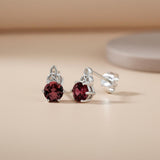 Sterling silver Celtic stud earrings with simulated rubies are shown on a neutral surface with a blurred background.