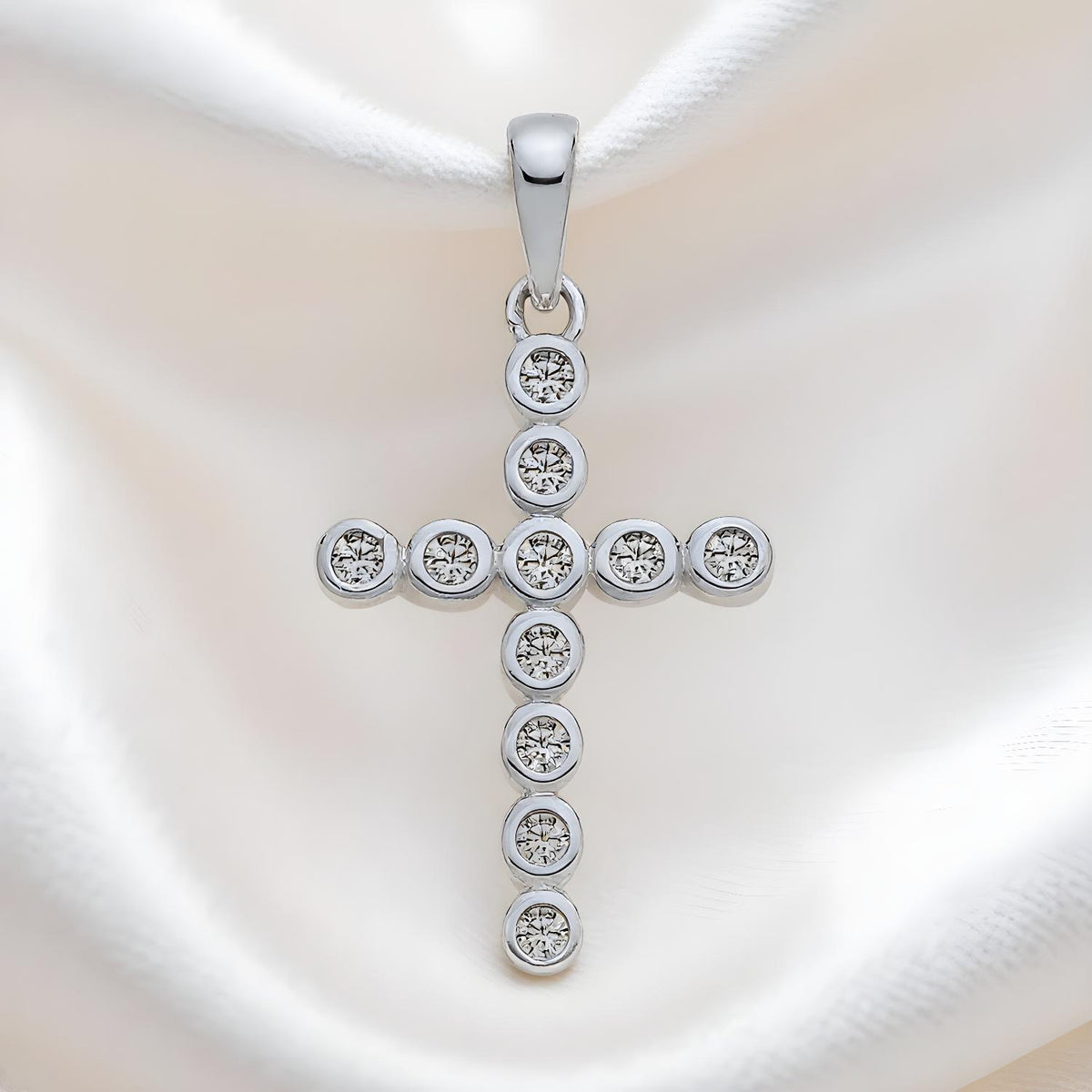 A Silversmiths sterling silver cross pendant with round-set CZ is shown resting on white satin fabric.