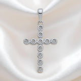 A Silversmiths sterling silver cross pendant with round-set CZ is shown resting on white satin fabric.