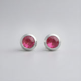 Sterling silver stud earrings with bezel-set simulated rubies on a minimalist light gray background.