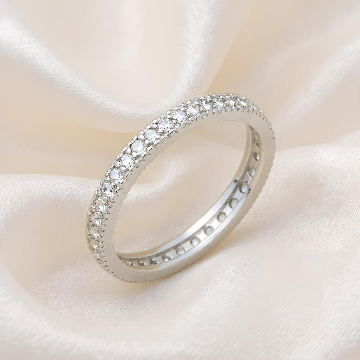 A sterling silver CZ eternity ring by Silversmiths rests on cream-colored satin fabric.