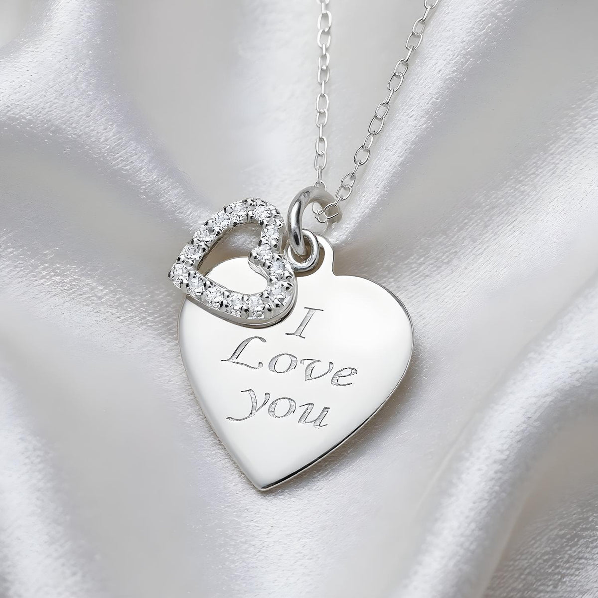 A Silversmiths sterling silver necklace with an “I Love You” heart charm and cubic zirconia on white satin fabric.