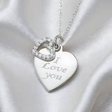 A Silversmiths sterling silver necklace with an “I Love You” heart charm and cubic zirconia on white satin fabric.