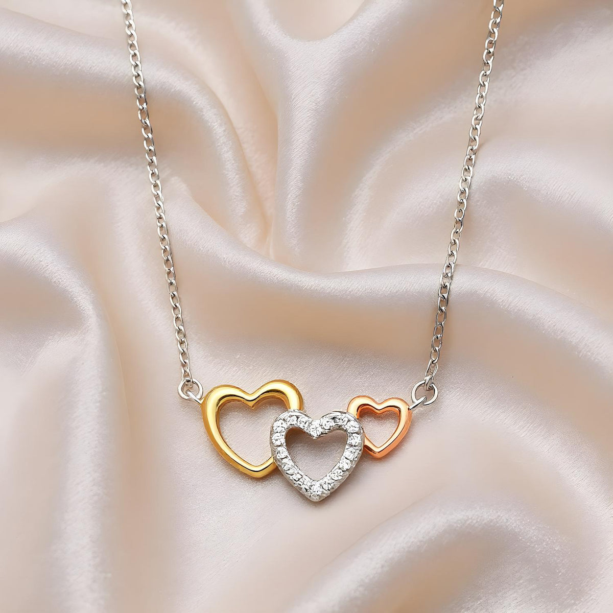 Triple Heart Necklace with rose, yellow, and silver hearts, each accented with cubic zirconia on ivory fabric.