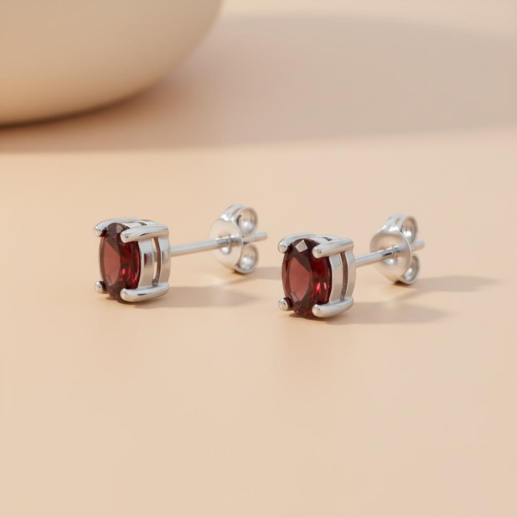Sterling silver stud earrings with oval natural garnets shown on a light beige surface.