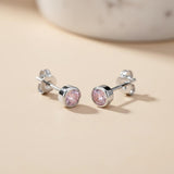 Sterling silver bezel studs with faceted simulated pink sapphires, displayed on a beige surface.