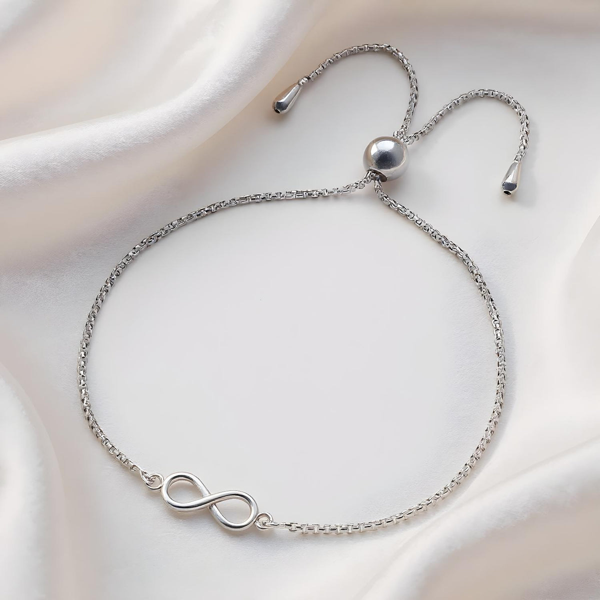A sterling silver infinity bolo bracelet from Silversmiths rests on smooth white satin fabric.