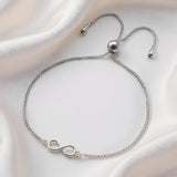 A sterling silver infinity bolo bracelet from Silversmiths rests on smooth white satin fabric.