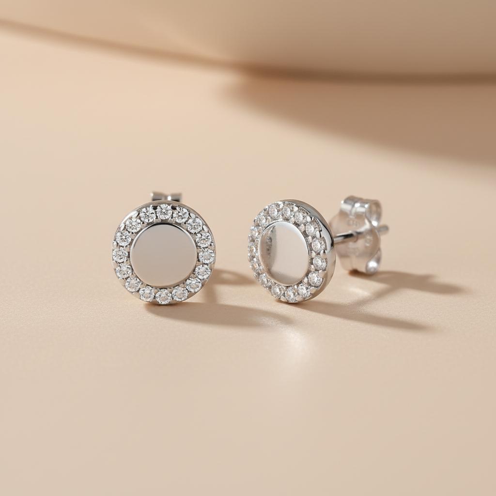 Silversmiths sterling silver stud earrings with cubic zirconia halo frames rest on a beige surface.
