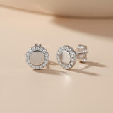 Silversmiths sterling silver stud earrings with cubic zirconia halo frames rest on a beige surface.