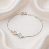 A sterling silver infinity station bracelet with adjustable links is shown on white fabric.