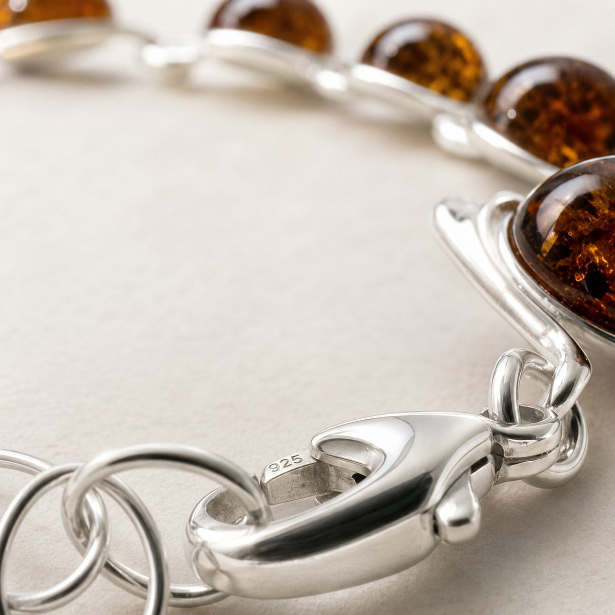 A silver bracelet clasp features Baltic amber stones set in linked ovals, shown close up on a light background.