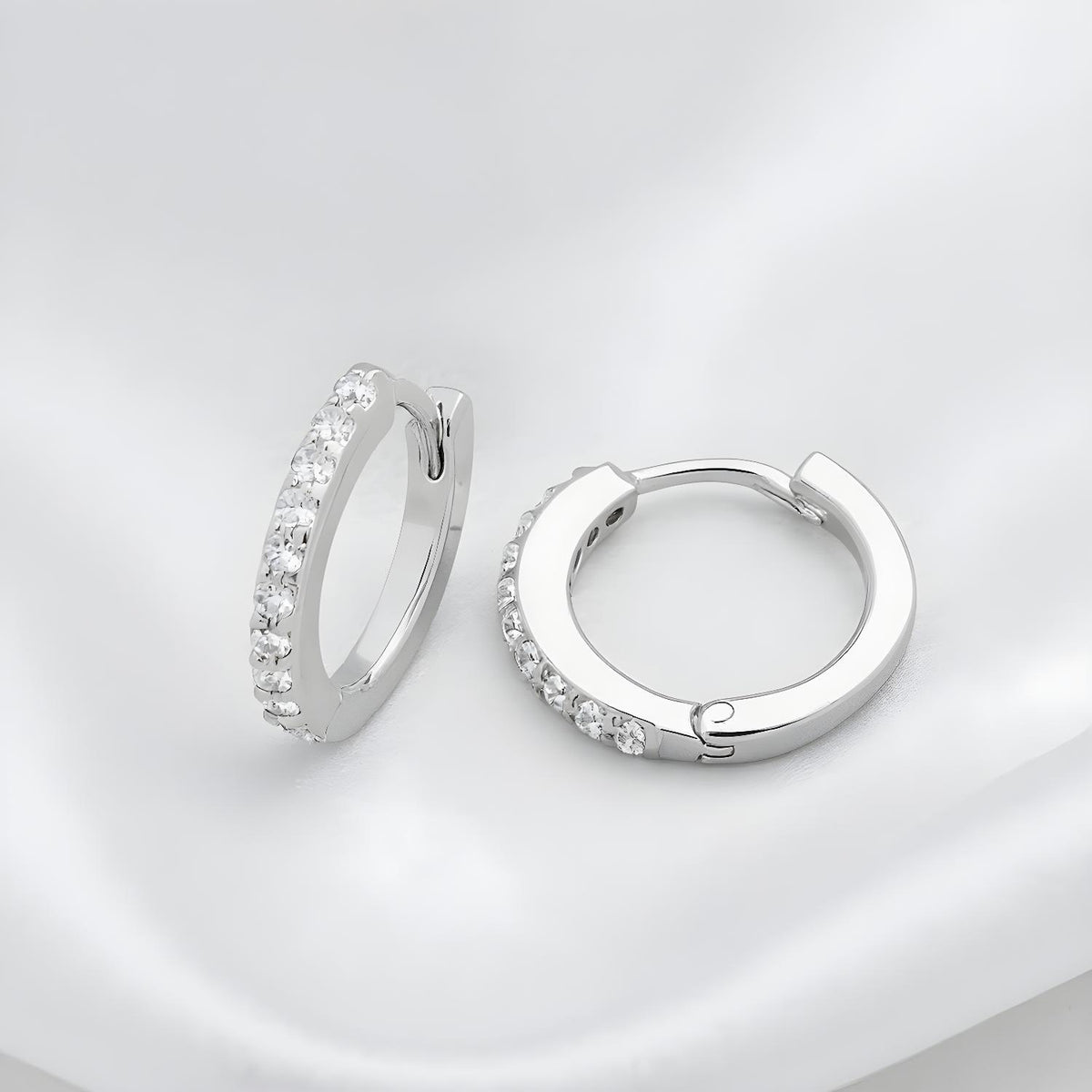Silversmiths sterling silver huggie hoops with cubic zirconia rest on a white fabric background.