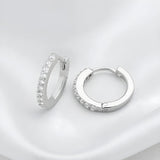 Silversmiths sterling silver huggie hoops with cubic zirconia rest on a white fabric background.