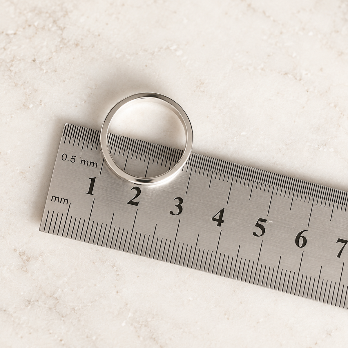 A silver ring rests on a metal ruler, showing its diameter measures exactly 2 centimeters.