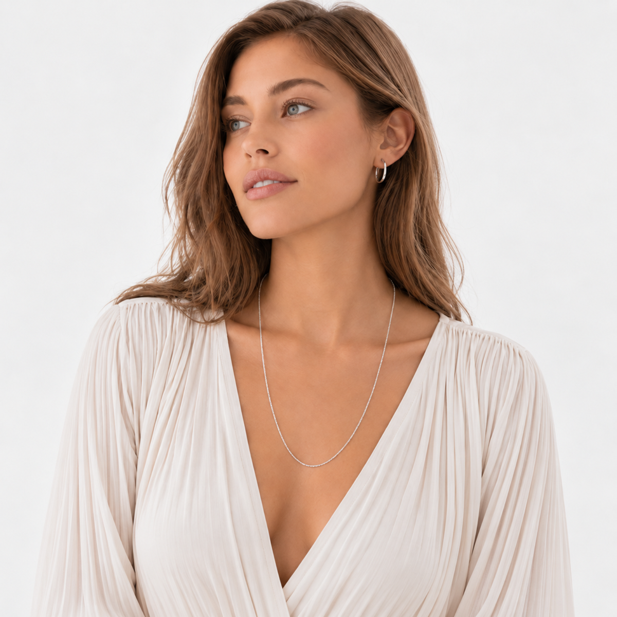 Woman wearing a white pleated dress, long silver necklace, and hoop earring.