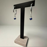 Sterling silver simulated sapphire charm hoop earrings displayed on a black T-stand with a wood base.