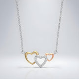 A sterling silver necklace with rose and yellow gold triple heart cubic zirconia pendant on a plain background.
