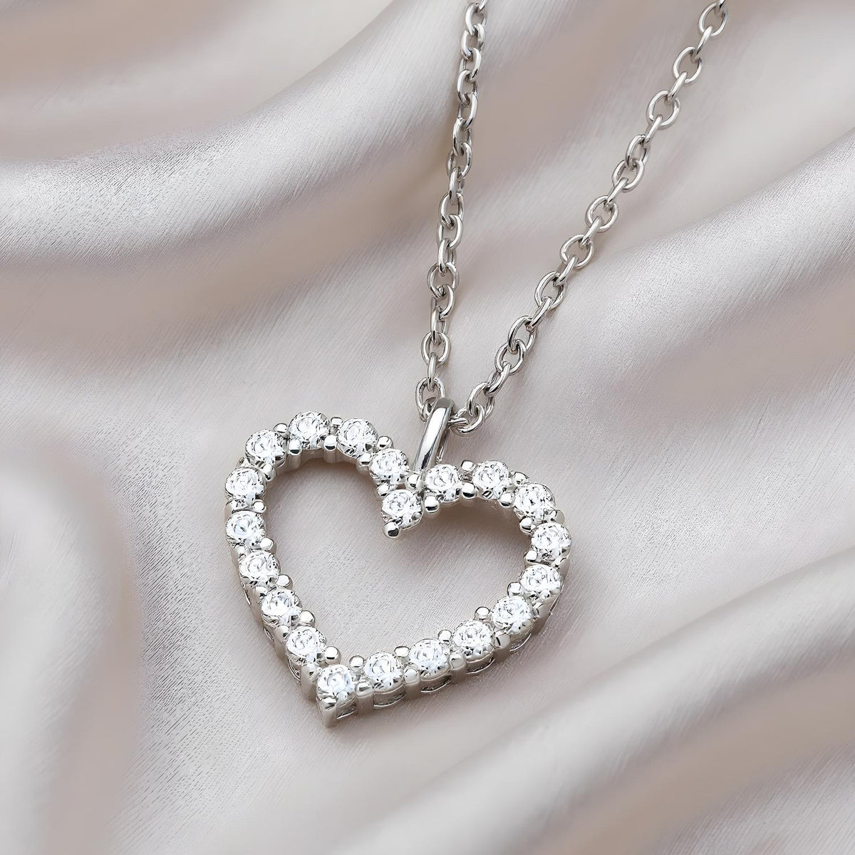 Sterling silver heart-shaped necklace with cubic zirconia, shown on a smooth, silky fabric background.