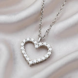 Sterling silver heart-shaped necklace with cubic zirconia, shown on a smooth, silky fabric background.