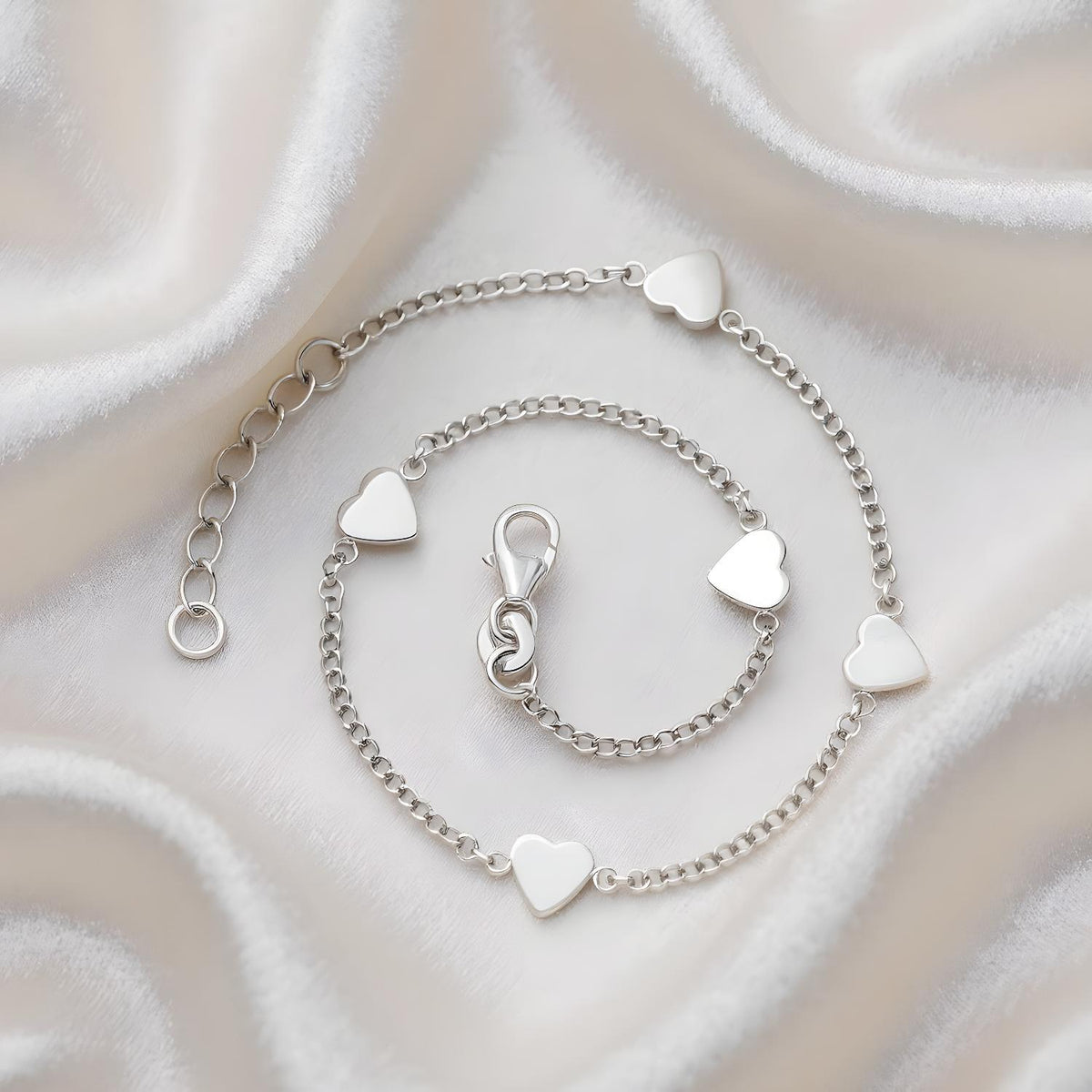 Sterling silver anklet with multiple heart stations and a lobster clasp, displayed on white satin fabric.