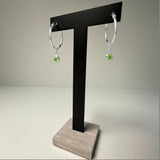 Sterling silver hoop earrings with simulated peridot charms displayed on a black T-stand with a wooden base.