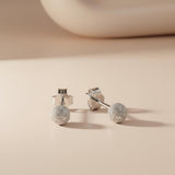 Silversmiths Sterling Silver 4mm frosted ball stud earrings rest on a smooth beige surface in soft lighting.
