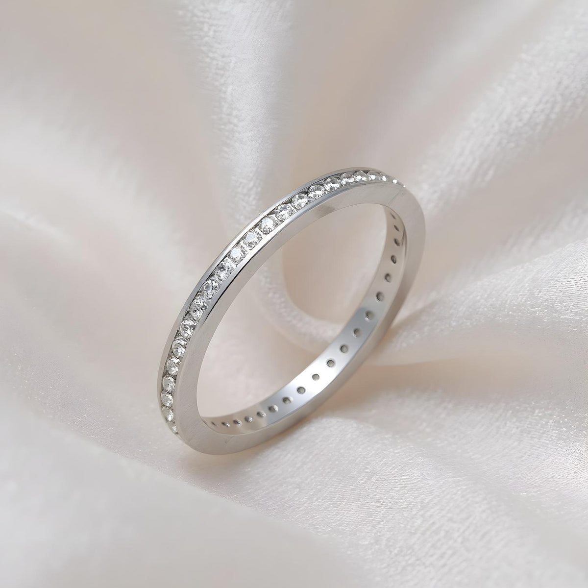 A Silversmiths sterling silver eternity ring with cubic zirconia rests on a soft, pale fabric background.