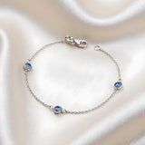 Sterling silver triple evil eye bracelet with blue stones displayed on a cream fabric background.