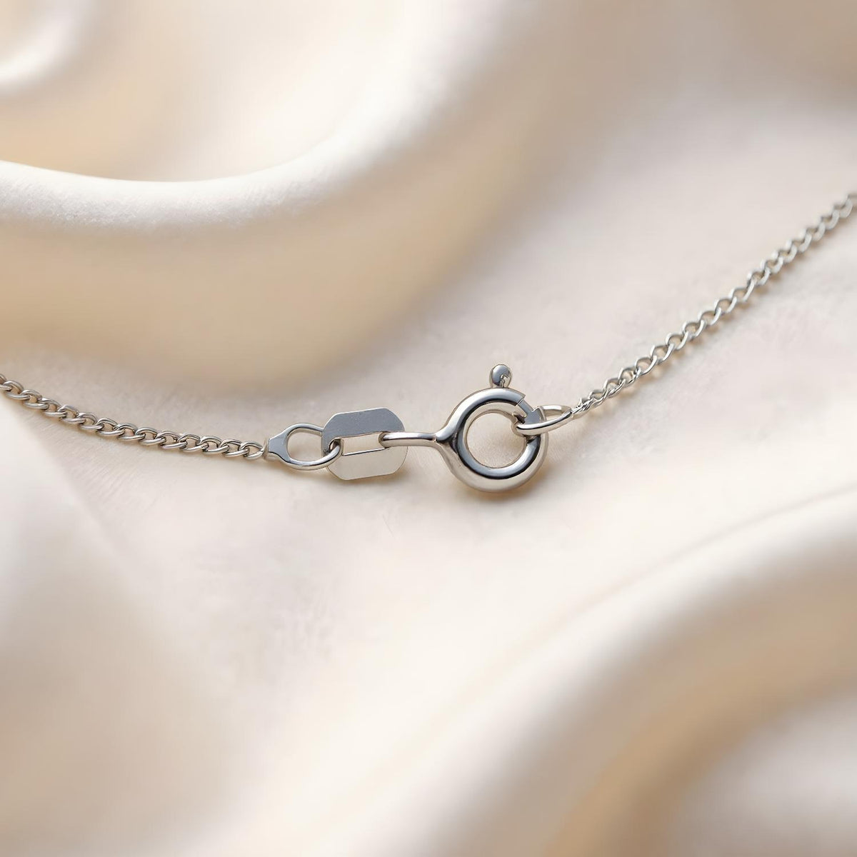 A 1.2mm sterling silver curb chain necklace with spring ring clasp displayed on cream fabric in close-up.