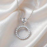 Sterling silver infinity love knot circle necklace with a cubic zirconia pendant, displayed on white satin.