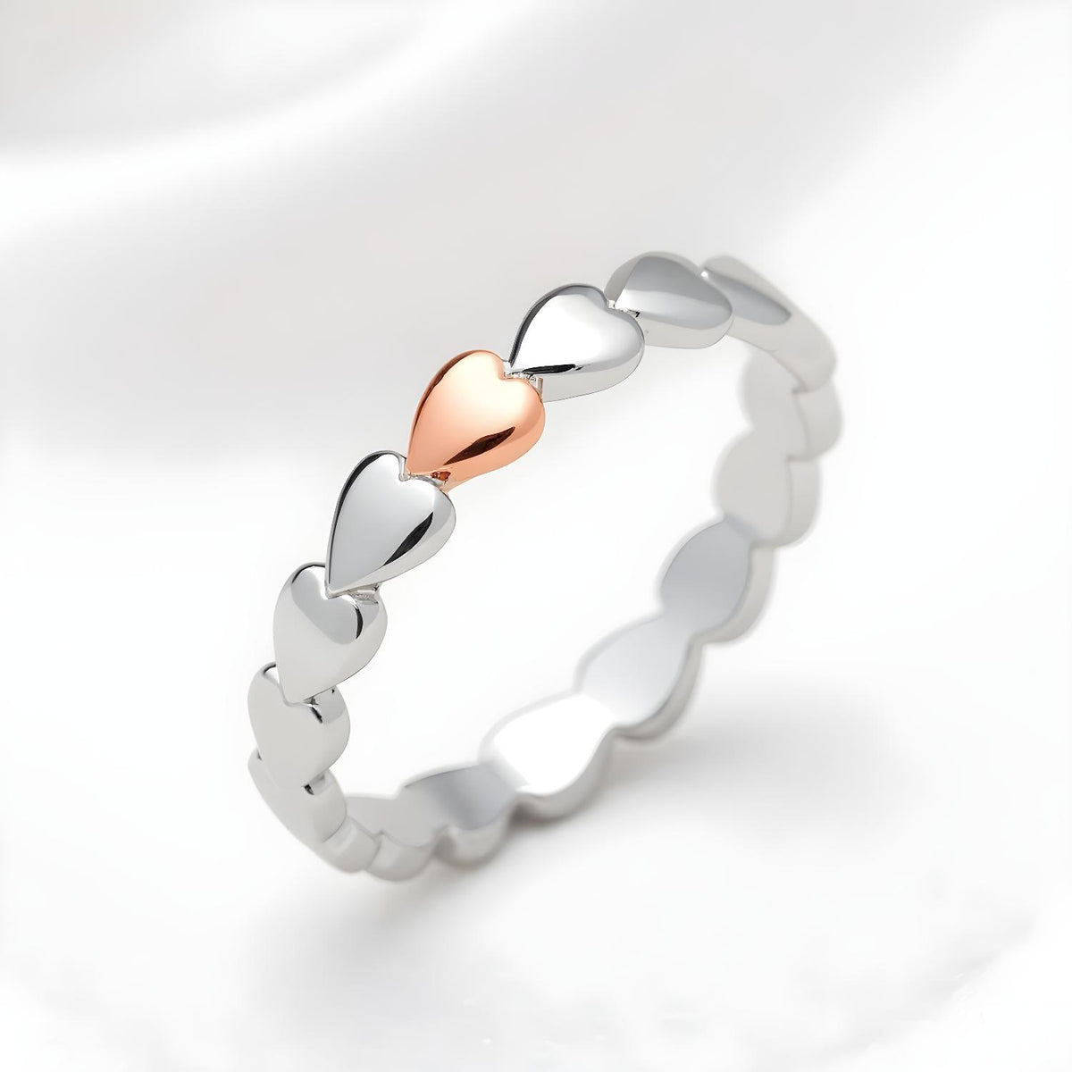 A sterling silver band ring with rose gold-plated heart design is displayed against a white background.
