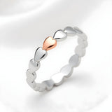A sterling silver band ring with rose gold-plated heart design is displayed against a white background.