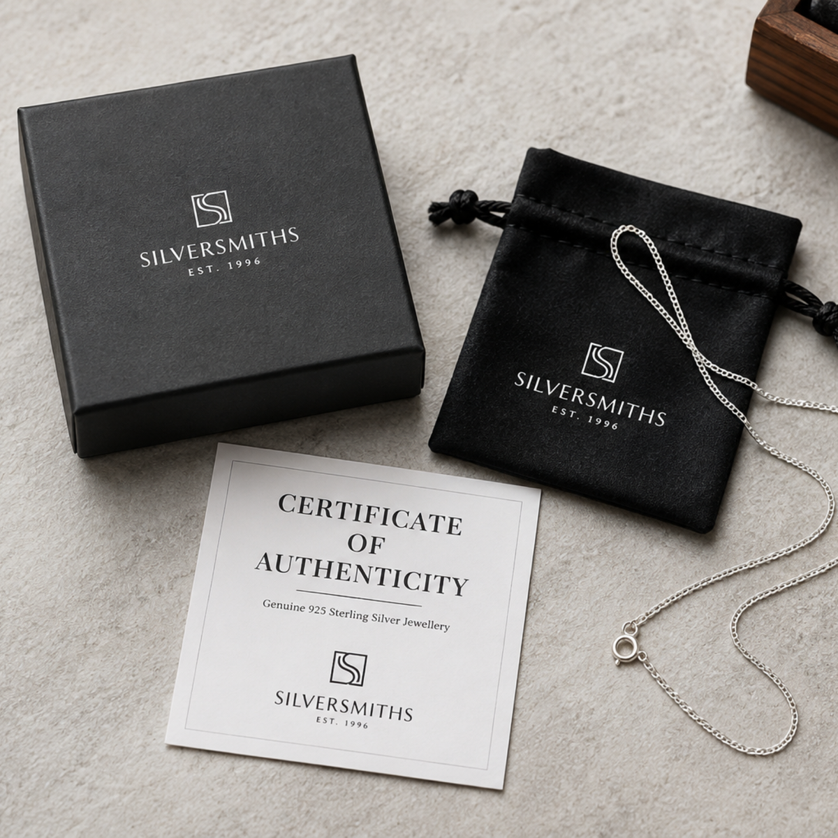A silver necklace with a Silversmiths certificate in a black pouch and box sits on a light surface.