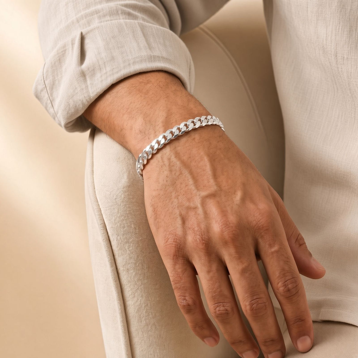 A hand with a silver chain bracelet rests on a light-colored upholstered chair.