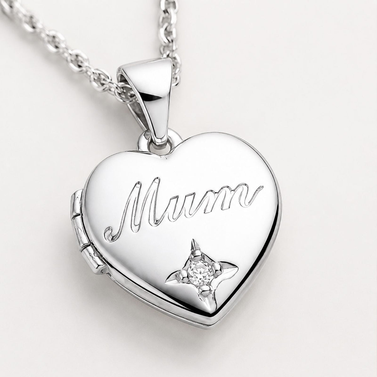 A silver heart-shaped locket necklace features “Mum” engraved on the front and a small diamond accent.