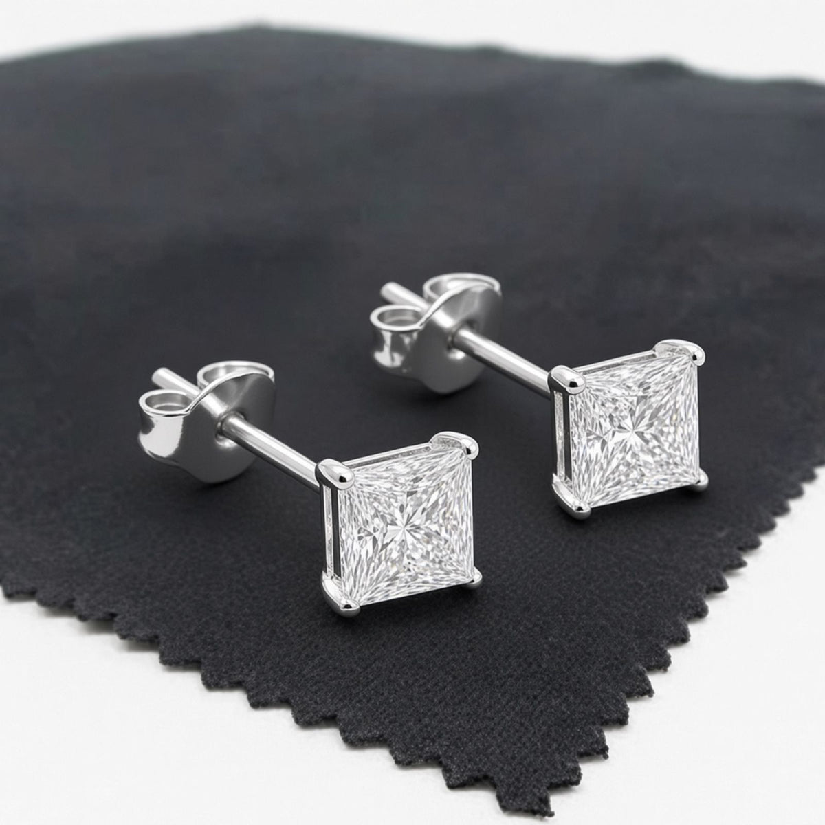 Square-cut diamond stud earrings displayed on black cloth, with facets catching the light.