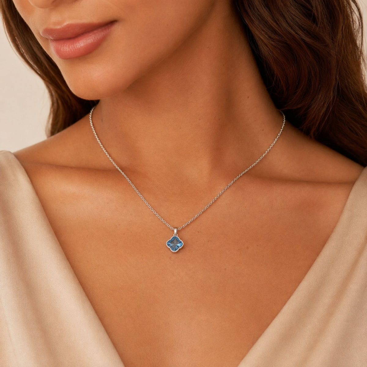 Woman in a light beige top wears a silver necklace featuring a blue gemstone pendant.